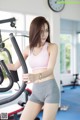 A woman in a pink top and gray shorts on a stationary bike.