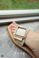 A woman's hand holding a watch on a window sill.