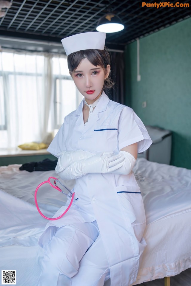 A woman dressed as a nurse sitting on a bed.