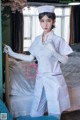 A woman dressed as a nurse standing in front of a bed.