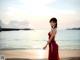 A woman in a red dress standing on a beach.