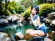 A woman in a blue and white outfit sitting on a rock by a river.