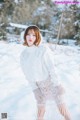 A woman in a white sweater and skirt standing in the snow.