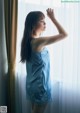 A woman in a blue dress standing by a window.