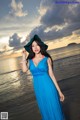 A woman in a blue dress and hat standing on a beach.