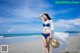 A woman in a blue bikini and a straw hat on the beach.