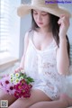 A woman in a white dress and straw hat holding a bunch of flowers.