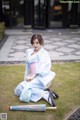 A woman in a blue and pink kimono sitting on the grass.