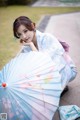 A woman in a blue kimono sitting on the ground holding an umbrella.