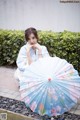 A woman in a blue kimono sitting on the ground holding an umbrella.