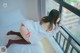 A woman in a white shirt and red stockings sitting on a bed.