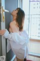 A woman in a white shirt and red stockings leaning against a door.