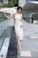 A woman in a white dress leaning against a glass wall.