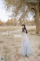 A woman in a blue dress standing in front of a herd of goats.