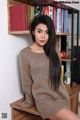 A woman sitting on top of a wooden shelf next to a book shelf.