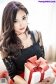 A woman in a black dress holding a white box with a red bow.