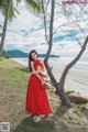 A woman in a red dress standing next to a tree.