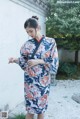 A woman wearing a blue and red kimono standing in front of a white wall.