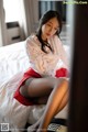 A woman in a white shirt and red skirt sitting on a bed.