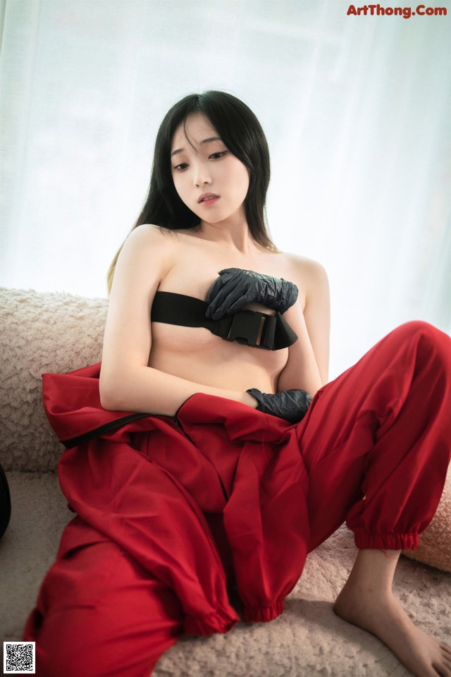 A woman in a black bra top and red pants sitting on a couch.