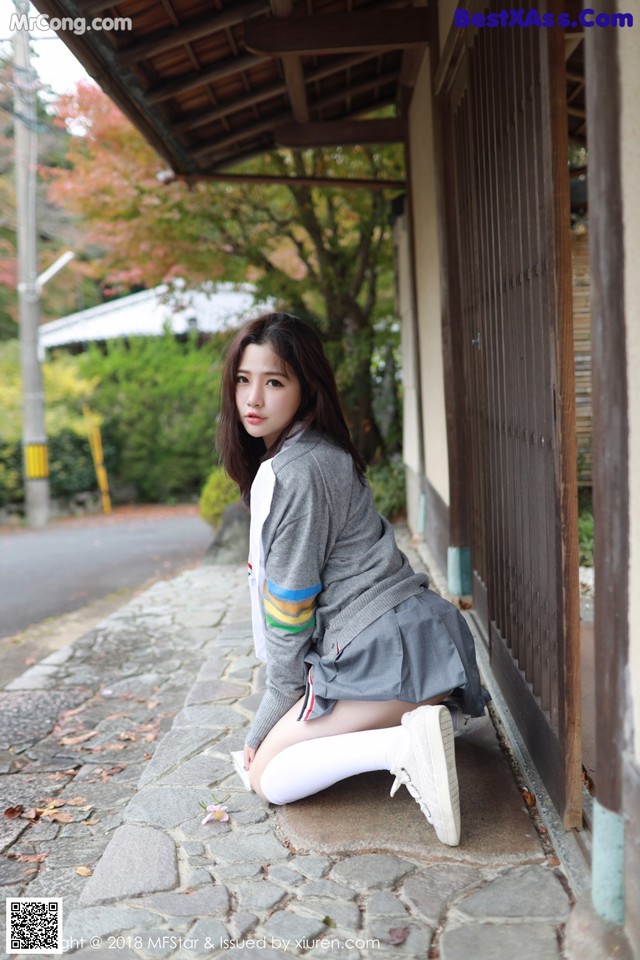 A young woman sitting on the ground in front of a building.