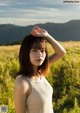 A woman in a white tank top standing in a field.